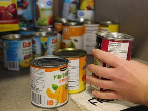 A staff member picks up a can of food from a shelf at Gleaners Food Bank. The annual report of a provincial food security group shows the pandemic is forcing more people to turn to food banks.