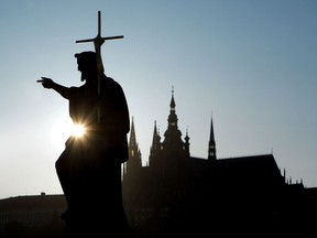 Silhouette of Saint John the Baptist statue from the Charles Bridge and St. Vitus Cathedral in Prague, Czech Republic.