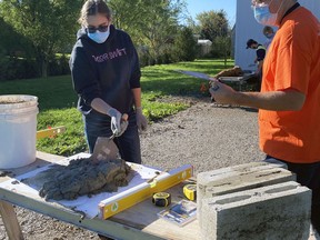 Ontario Masonry Training Centre instructor Christopher Mayberry shows MDHS student Alley Kemp (left) how to handle mortar with a trowel during a recent visit to the school. SUBMITTED