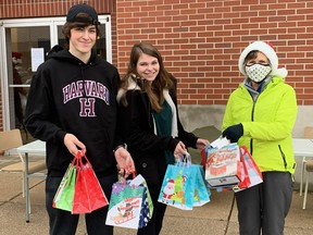 Upon learning that Church Out Serving was staging its second annual  Christmas banquet in Simcoe this weekend, Jayden Winter and Matthew Kraemer, left, prepared gift bags of chocolates, socks, hand-warmers and other useful items for the Christian outreach group to distribute to those in need. Happy to accept the donation, at right, was Church Out Serving volunteer Pat Earls. – Church Out Serving photo