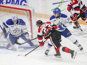 Will Gerrior of the Ottawa 67's avoids a check by Nolan Collins (77) and shoots the puck at netminder Mitchell Weeks of the Sudbury Wolves during an Ontario Hockey League game at TD Place arena on Jan. 15, 2022.