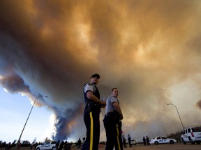 Police officers direct traffic under a cloud of smoke from a wildfire in Fort McMurray, Alta., on Friday, May 6, 2016. Jason Franson/The Canadian Press