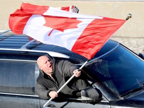A man waves a large Canadian Flag outside the passenger window of a vehicle taking part in the "Freedom Convoy" protest against vaccine mandates, as it approaches the Stewart Boulevard overpass on Highway 401 in Brockville, Ont., Friday morning, Jan. 28, 2021. (RONALD ZAJAC/The Recorder and Times)