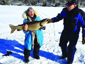 Salli Watson struggles to hold up the lake trout she caught on Saturday, Feb. 20 on Ten Mile Lake, located just west of Dunlop Lake. She got help reeling in and holding up her catch from a nearby angler, Chuck Anderson.