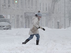 A woman walks over snowbanks at the corner of Princess and Wellington streets in Kingston on Monday. Kingston was due to receive between 25 and 40 centimetres of snow.