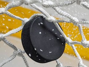 A close-up view of an Ice Hockey puck hitting the back of the goal net as shavings fly by, viewed from the front. Scoring a goal in ice hockey.