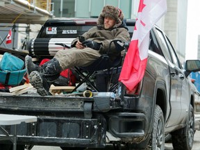 A man relaxes in his pickup truck as truckers and supporters continue their protest in Ottawa on Sunday. The negative impacts on local businesses have been far-ranging.