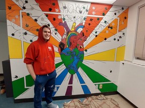 Sam Barry stands in front of a mural he created on a wall at the Pride office at Laurentian University.