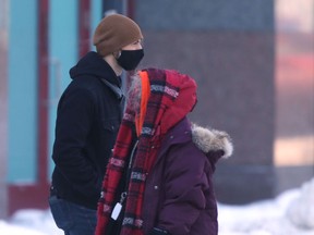 Two people wear masks while walking along a sidewalk in Winnipeg on Friday, Feb. 11, 2022.