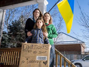 Corinne Sykes, left, and her partner Myroslava Symonenko, stand behind their 12-year-old son Gordiy Symonenko as he holds a donation box which sits in front of the family's home. Thursday in Belleville, Ontario. ALEX FILIPE