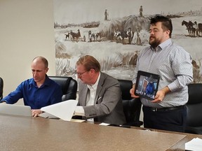 Frank Louvelle of the Cochrane Board of Trade is joined by Marc Kealy of KPGI and virtually by Chief Keith Matthew of the Indigenous Critical Infrastructure Fund (being displayed by Jason Michaud Master of Ceremonies) as they sign  the Tri-partite agreement which would move a project forward to making the community a sustainable model for power and food production.