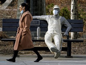 A woman walks past a statue wearing a face mask in Edmonton during the COVID-19 pandemic on April 14, 2021. PHOTO BY LARRY WONG / Postmedia, file.