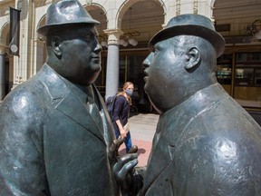 A woman wearing a protective mask walks past the statues of two businessmen on Stephen Avenue Mall in downtown Calgary in May 2020. (Postmedia file photo)