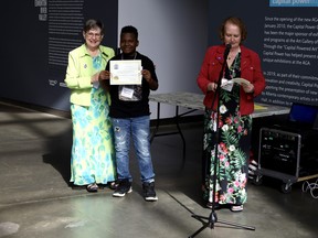 Grade 5 St. Thomas Aquinas Catholic School student Zachariah Morrison (centre) recieves a certificate from Lynne Duiguo (left), President of the Alberta Genealogical Soceity (AGS), for his participation in the school's 'Our Family Roots' project created by teacher Marion Rex (right) at the Art Gallery of Alberta (AGA) in Edmonton on Sunday, Mar. 27, 2022. Photo by Rudy Howell/Postmedia.