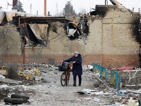 A woman walks with a bicycle next to a building damaged during Ukraine-Russia conflict in the separatist-controlled town of Volnovakha in the Donetsk region, Ukraine, Tuesday, March 15, 2022.