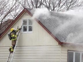 A firefighter breaks a window to provide some ventilation to a house that caught on fire on Inshes Avenue in Chatham on Monday. (Ellwood Shreve/Chatham Daily News)