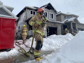 A Kingston Fire and Rescue firefighter carries a hose from the scene of an early morning house fire on Pauline Tom Avenue in Kingston, Ont., on Wednesday, March 2, 2022. Elliot Ferguson/The Kingston Whig-Standard/Postmedia Network