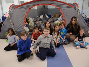 Windsong Heights grade 2 students Anuki (from left to right), Dax, Masanobu, Monique, Brielle, Cohen and Lexi sit with Mrs. Data in front of a tent filled with the food donations generated by students that went to the Airdrie Food Bank. Photo by Riley Cassidy/The Airdrie Echo/Postmedia Network Inc.