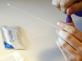 A person holds a swab while sealing a container of testing solution during a rapid antigen test for COVID-19.