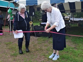 Marion French cuts the ribbon to herald another season of the Powassan Farmers' Market.  French and her late husband Robert were among the founding members of the annual event 34 years ago.   A steering committee made up of several local residents was formed in the late 1980s to explore starting a farmers' market.   Also pictured is JoAnn Long, the chair of the Powassan Farmers' Market, continuing a tradition to open farmers' markets with a bell ringing.