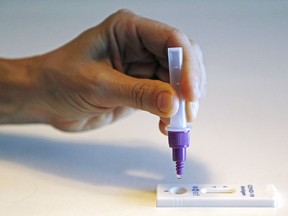 A person squeezes a drop of testing solution into a COVID-19 rapid antigen testing device.