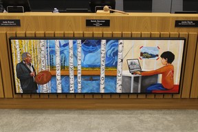 Teachings by Frederick McDonald hangs inside the council chambers at the Jubilee Centre in Fort McMurray on April 25, 2022. An elder on the left continue sharing their teachings with stories and drums. The thunderbird on the drum symbolizes a connection to the spiritual world, painted stylistically with a red dress symbolizing missing and murdered Indigenous women and girls. A girl on the right learns about Residential Schools next to a picture of a train some used to reach trap lines. The middle background is a reference to past modes of transportation. “All these parts speak of or shared histories,” writes McDonald. “In spite of it all and of all the generations of colonial presures we are still strong peoples—growing stronger through understanding!” Vincent McDermott/Fort McMurray Today/Postmedia Network
