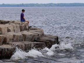 A man stares out across Lake Ontario while sitting on top of some rocks in Breakwater Park in Kingston on Tuesday.