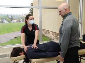 Professor Yves Charette, of the massage therapy program at College Boreal, looks on as graduate student Melanie Trottier treats soccer player Cohen Frappier at Ecole secondaire Sacre-Coeur in Sudbury, Ont. on Thursday May 26, 2022. Charette and four graduate students from the program will be offering their services to caddies at the RBC Canadian Open in Toronto. The tournament runs from June 6 to 12. John Lappa/Sudbury Star/Postmedia Network