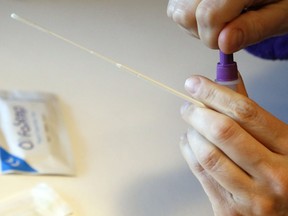 A person holds a swab while sealing a container of testing solution during a rapid antigen test for COVID-19.