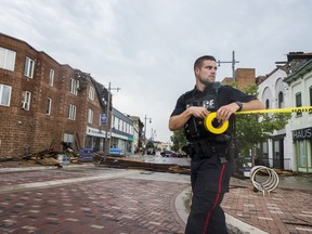 A Belleville police officer rolls out caution tape after portions of a roof were ripped off of a downtown Belleville business during heavy winds on Thursday. ALEX FILIPE