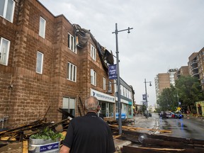 A property owner inspects the damage done to building after pieces of a roof were hurled into the facade of the structure during high winds on Thursday. The cleanup continued Friday.
