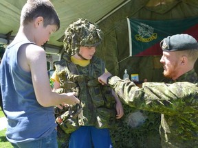 Cpl. Jason Gaynor of the Grey and Simcoe Foresters helps nine-year-old Reid Brown into a fragmentation vest, tactical vest and helmet during the Billy Bishop Heritage Fest at the Billy Bishop Museum in Owen Sound, Ont., on Saturday, June 18, 2022. Looking on is eight-year-old Connor Luckie.