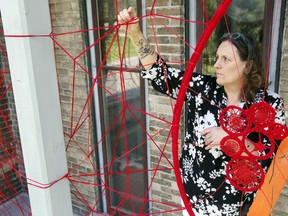 Hamilton-based Metis artist Tracey-Mae Chambers creates an installation using red yarn Tuesday on the front veranda of Glanmore National Historic Site in Belleville. People's questions about the installations lead to discussions about decolonization, she said.