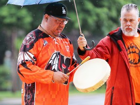 Sarnia city Coun. Brian White holds an umbrella while Nim Plain, from the Aamjiwnaang First Nation, performs Monday during a dedication ceremony for a new orange Cathcart Boulevard crosswalk, commemorating Indigenous children taken from their families and forced into residential schools. (Terry Bridge / Sarnia Observer)