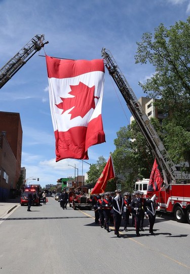 A huge Canadian flag hangs from fire truck ladders at a funeral procession for Greater Sudbury firefighter Mike Frost in downtown Sudbury, Ont. on Wednesday June 1, 2022. His obituary said, "It is with deep sorrow and great sadness that the family of Mike Frost announce his unexpected death at his residence on May 19, 2022, at the age of 40." John Lappa/Sudbury Star/Postmedia Network