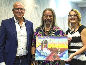 First Nations artist Michael Cywink, holding one of his paintings, is flanked by Rod LaRoque, president of IINTA and the local Human League chapter, and Anne Salter, executive director of the Sudbury-Manitoulin Children's Foundation. The Playing for Change series of events begins Aug. 8 with an art show at Science North, which will be preceded by a silent digital auction. Supplied