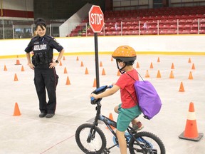 Timmins Police auxiliary officer Tammy Grydsuk checks to see that a young cyclist, Austen Hookimaw, is properly stopped at a stop sign.  His new helmet was provided to the event at cost by O'Reilly Source for Sports.  NICOLE STOFFMAN/The Daily Press