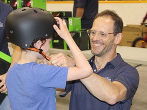 Yves Viel, left, law clerk and bookkeeper at Girones, Bourdon Kelly, fits a new helmet onto the head of young cyclist Mikael Croussette during the Helmets on Kids bike rodeo held Thursday at the Archie Dillon Sportsplex.. A properly fitted helmet worn by every The cyclist could prevent four out of five injuries, according to the Porcupine Health Unit.  NICOLE STOFFMAN/The Daily Press