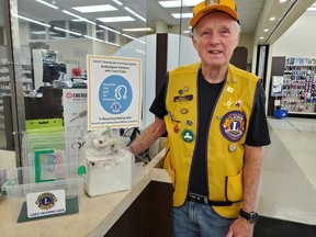 Findlay Barr of the Cochrane Lions Club stands beside the deposit box at Wallace Drug Store. The Club have been collecting used hearing aids for those who otherwise would not be able to get them.