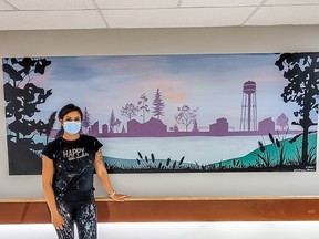 Ashley Rosenow, owner of Illustrious Interiors, poses with the mural she painted at the Heartland Community Hospice. Photo Supplied.