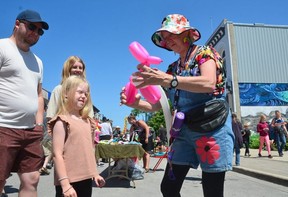 Zoey Laurin makes a balloon dog for 7-year-old Ciara Oldrieve at the hottest street sale along East 2nd Avenue on Saturday July 9, 2022 in Owen Sound, Ont.  It was the 32nd edition of the event and the first time it has been held since 2019. Ciara's parents, Nick and Kaela Oldrieve, look on.