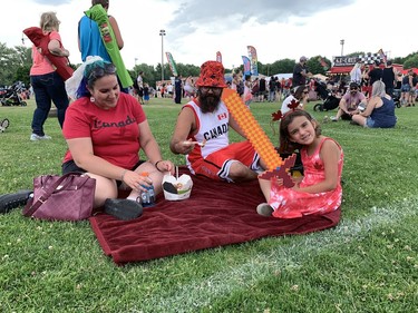 Stephanie Brown, Kyle Saunders and Amelia Saunders share a poutine snack during Brantford's Canada Day party on Friday. Susan Gamble