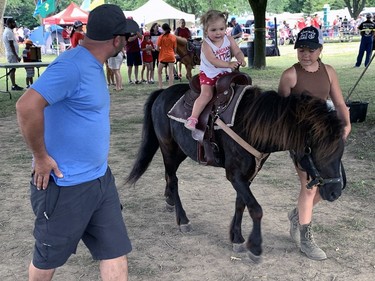 Sporting a shirt that says "Canadian Cutie," Blakely Neiman, 2, goes for a ride, guided by Natasha Smith, while her dad, Tyler Nieman, accompanied her at the pony ride station that was part of Brantford's Canada Day party on Friday. Susan Gamble