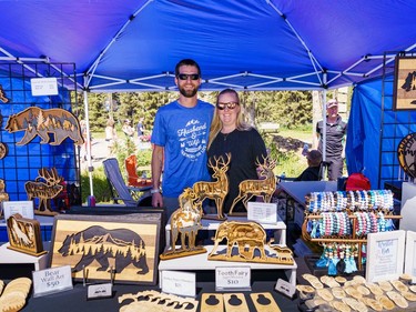 Matt and Ashley Babb pose for a portrait in their booth at the Bragg Creek Days market in Bragg Creek on Saturday, July 16, 2022. Ashley Babb uses a CO2 laser cutter to create different designs in wood.