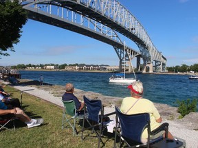 Spectators watch from the shore in Point Edward near the Blue Water Bridge Saturday as a sailboat on the St. Clair River heads for Lake Huron for the start of the annual Port Huron to Mackinac Island sailboat race.