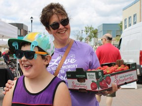 Janice Vickers and her son, Mason, smiling after purchasing a flat of strawberries from Sunrise Orchards, one of the vendors that were set up in the Urban Park for the downtown farmers' market held Thursday.  NICOLE STOFFMAN/The Daily Press