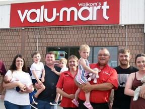 After 19 years as franchise owners, Steve and Terry Walkom have sold the grocery store business and retired as of July 17. Their extended family gathered outside the store for a group photo recently, and include (from left): Elaine White, son Kevin, daughter Jenna Siemon holding Caden, Carter, James and Cohen, Terry, Steve holding Emma, son Joe, and Shannon McKone holding Everett. ANDY BADER/MITCHELL ADVOCATE
