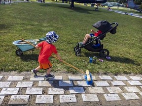 Eli Atkinson pushes a broom as he cleans off Ad Astra memorial headstones while his brother Joel sits in a stroller behind him. Submitted.