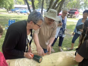 Colleen Stockford (left) carves the Communities in Bloom logo into a log. Omar Sherif / The Journal