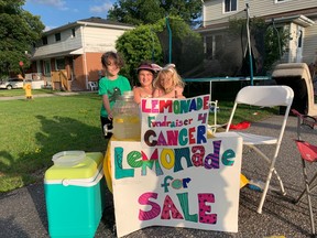 Skyla Sterling, 10, poses with her friends beside her, Ashton Conroy, 6, and Ava Conroy, 8, Thursday evening at her lemonade stand on Trout Lake Road. The youth is raising money for cancer research.